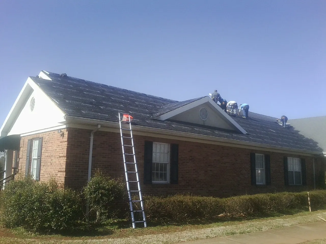 Crew tearing shingles off a brick ranch roof with a ladder set — Metal Roof Repair work by our crew in Bradfordsville