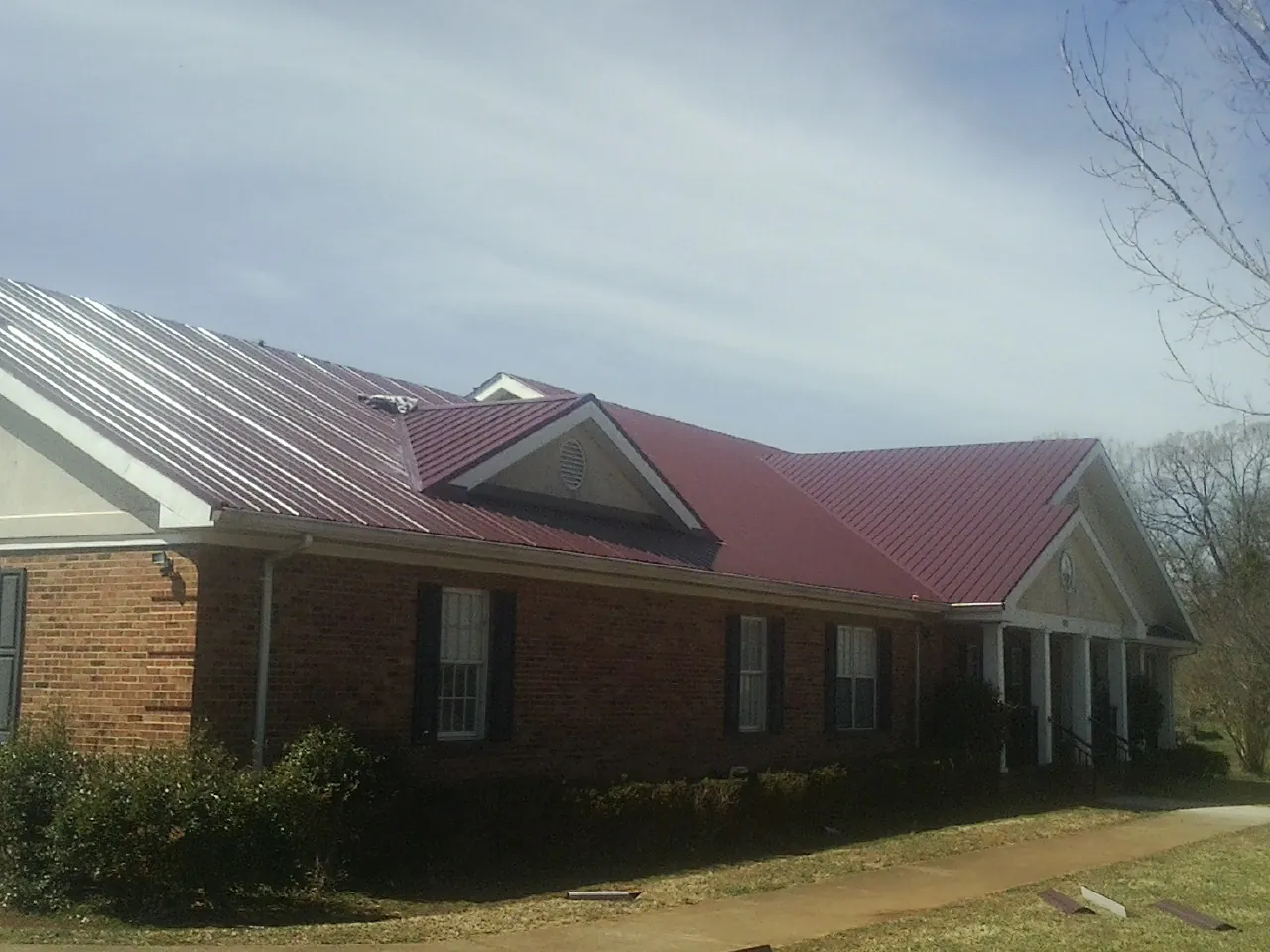 Red metal roof with gabled entries on a long brick building, from a Hail Damage Roof Repair job in Bradfordsville
