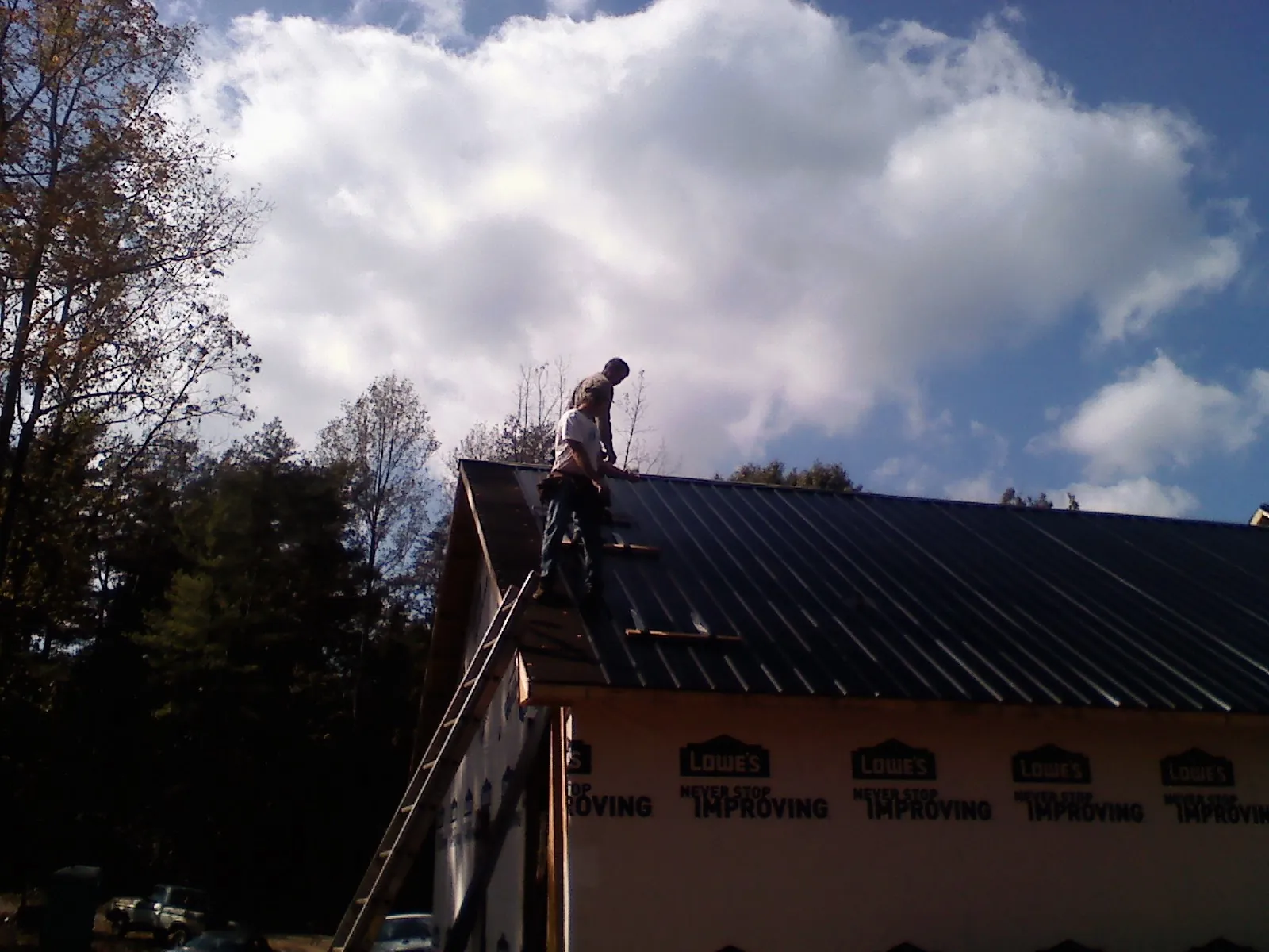 Roofer fastening dark metal panels high against a cloudy sky, from a Roof Inspection job in Bradfordsville