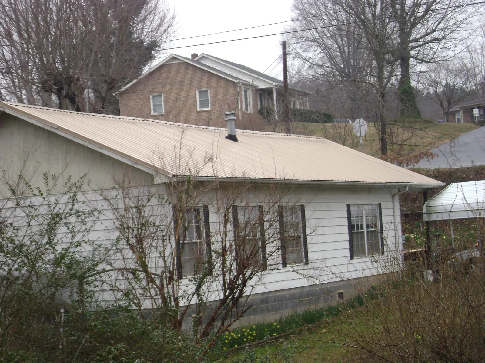 Tan metal roof on a white sided house set into a hillside — Commercial Roofing by Roofing Brothers in Bradfordsville