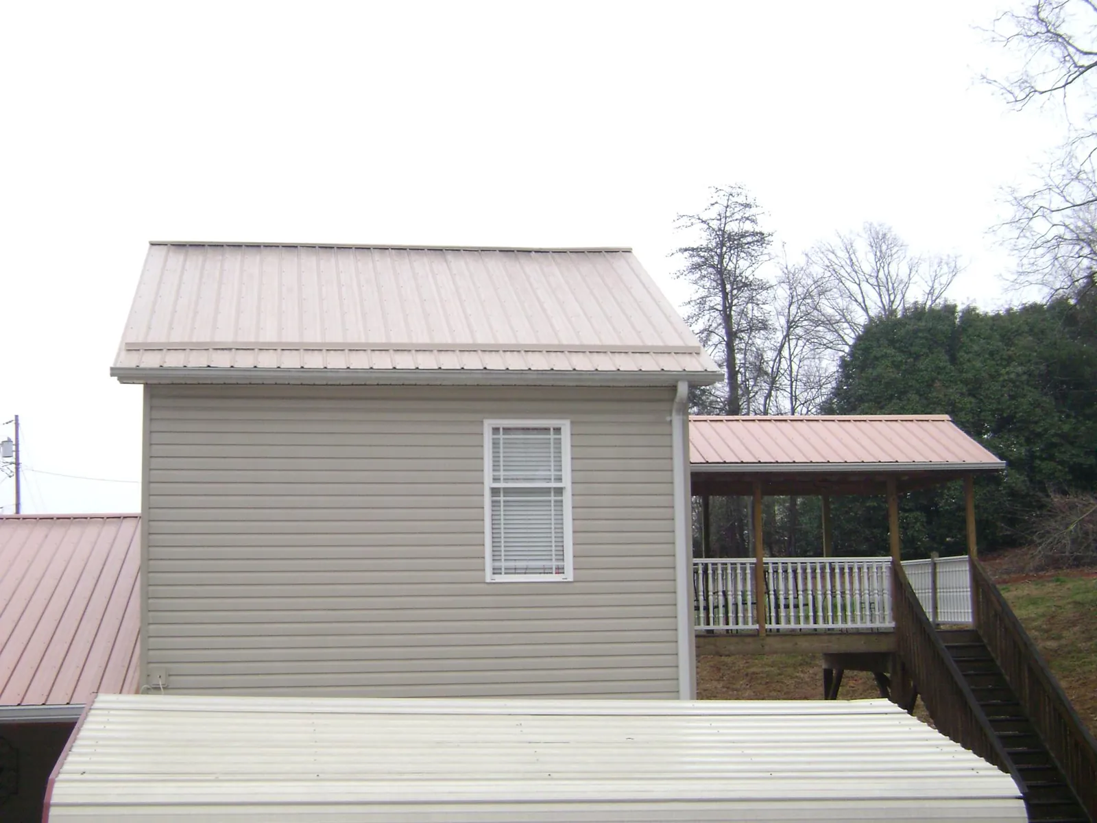 Tan metal roofs on a two story addition and attached porch, from a Roof Replacement job in Bradfordsville